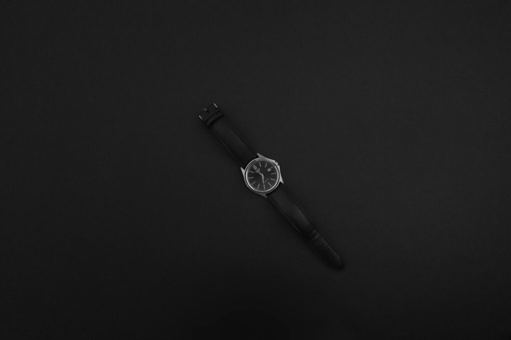 A classic wristwatch with a leather strap on a black surface, showcasing minimalist elegance.