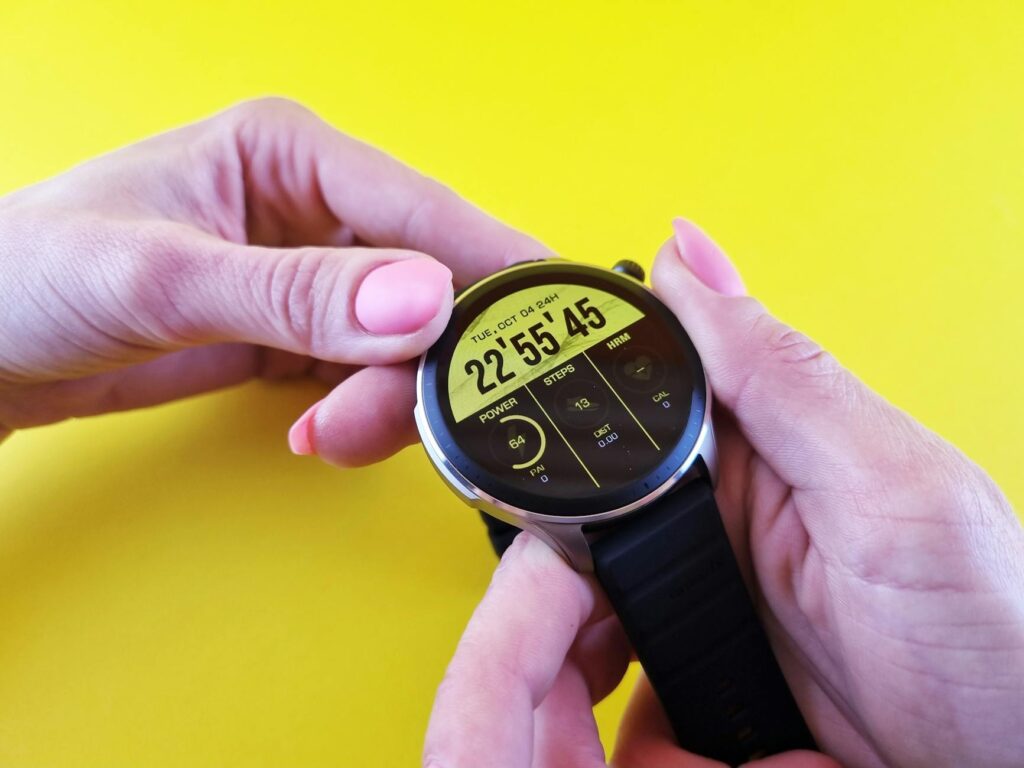 Close-up of hands holding a sleek smartwatch, highlighting technology against a bright yellow background.