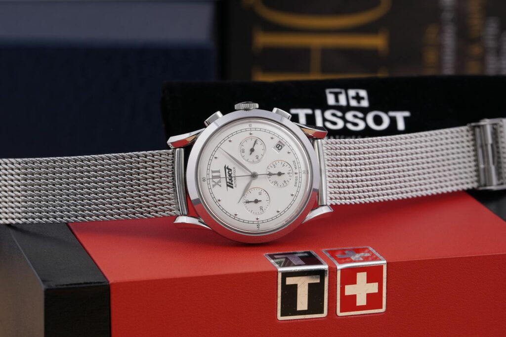 Silver wristwatch with mesh band elegantly displayed on a red box, highlighting luxury and style.